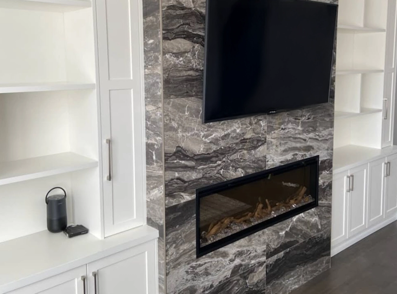 Custom white built-in shelving flanking a dramatic marble fireplace wall with TV