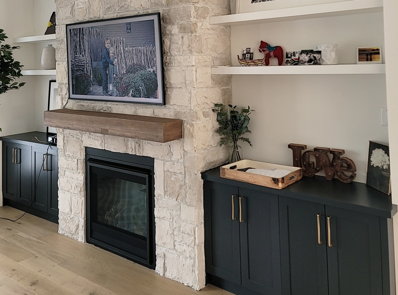 Custom dark navy built-in cabinetry flanking a stone fireplace with floating shelves