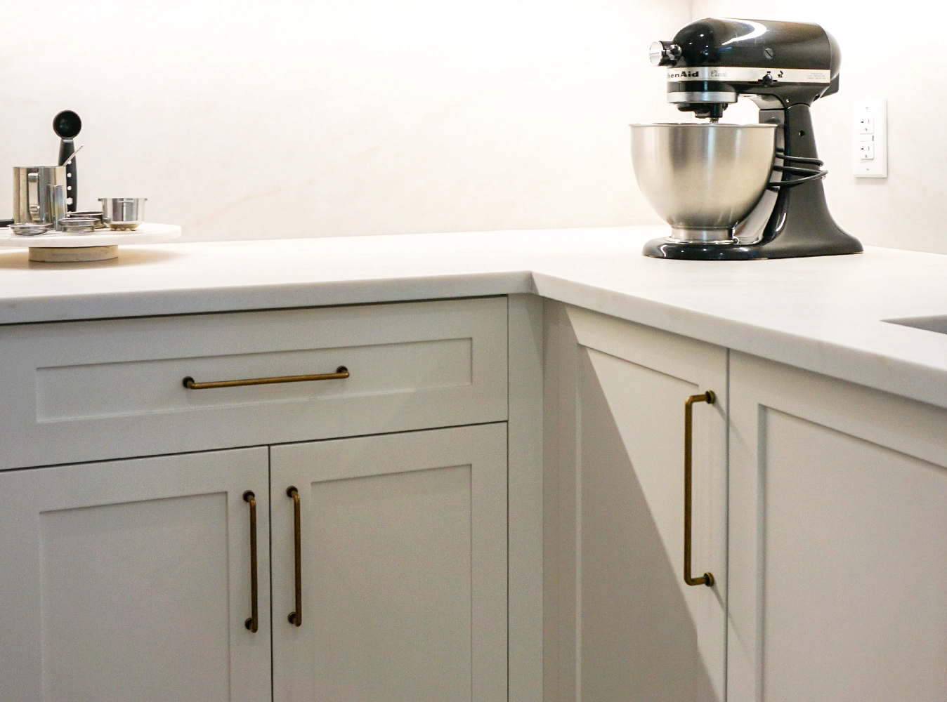 Painted sage shaker cabinetry with antique brass pulls and marble backsplash